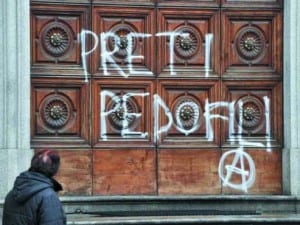 Una scritta contro i preti pedofili sul portone di una chiesa.