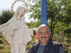 Paolo Brosio sulla collina delle apparizioni di Medjugorje, vicino ad una statua della Madonna.