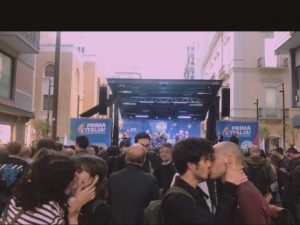 Il bacio fra una coppia di ragazze e una di ragazzi stagliato contro il palco del comizio di Matteo Salvini.
