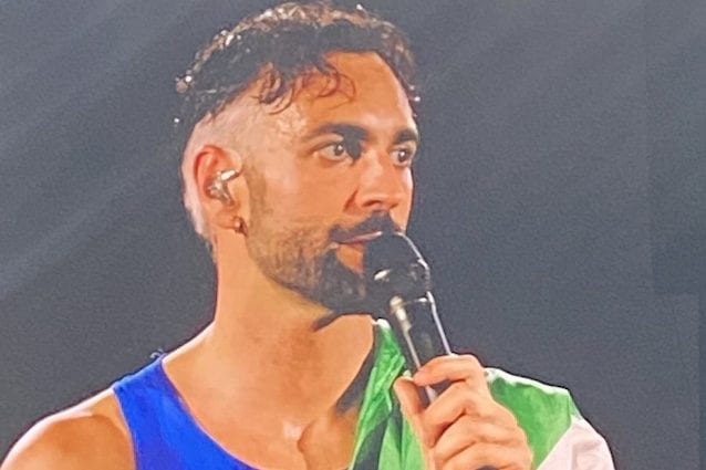Mengoni che parla al pubblico di Napoli con la bandiera della Palestina sulla spalla
