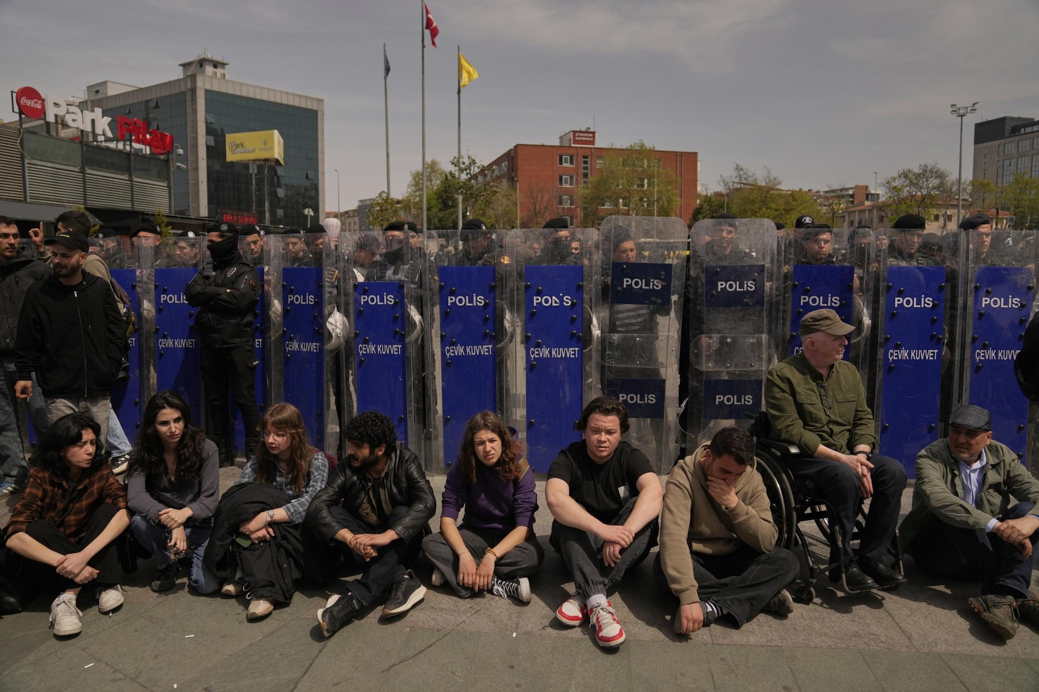 Persone sedute accanto alla linea di sicurezza della polizia durante una protesta fuori dal tribunale di Caglayan, a Istanbul. Credit: AP Photo/Khalil Hamra