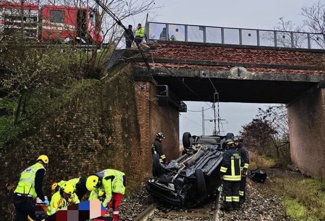 Auto cade dal cavalcavia e si schianta sui binari a Piacenza: 2 feriti, treno fermato appena in tempo