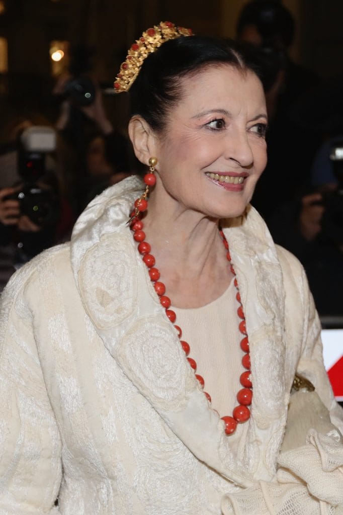 Carla Fracci con gioielli rossi che spiccano sul cappotto bianco