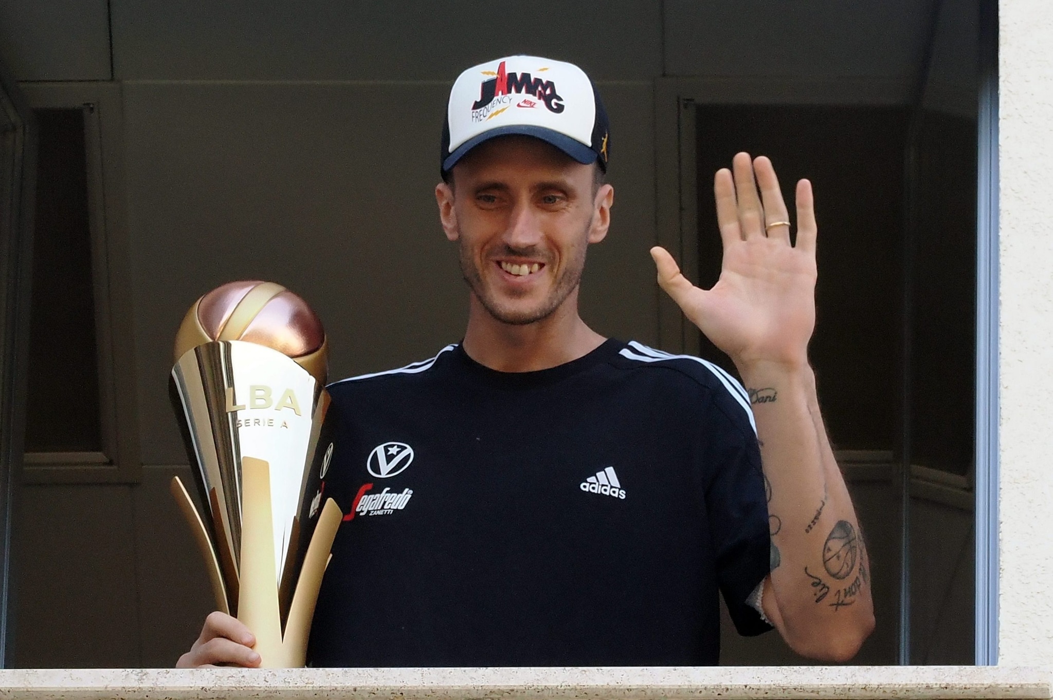 Achille Polonara si affaccia dalla sua stanza d’ospedale a Bologna col trofeo dello Scudetto della Virtus Bologna