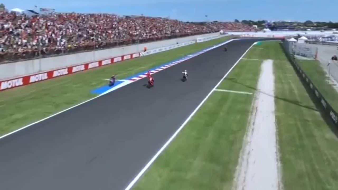 Jack Miller (a sinistra) sfila contromano sul tracciato di Misano mentre Marc Marquez festeggia la vittoria della gara con il suo tradizionale bandierone.