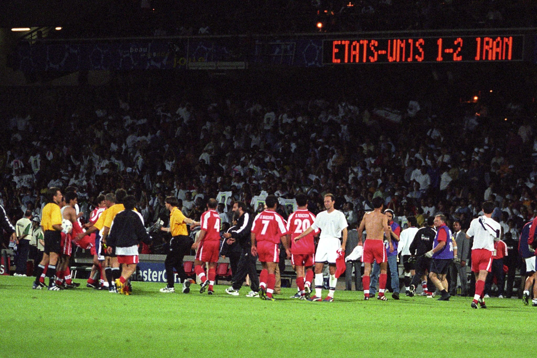 I calciatori di Iran e USA dopo il fischio finale e il tabellone dello Stade de Gerland con il risultato finale.