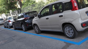 Auto parcheggiate negli stalli delimitati dalle strisce blu, con una Fiat Panda bianca in primo piano.