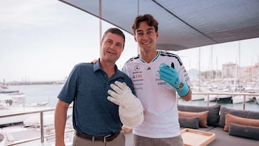 Reid Wiseman e George Russell sorridono insieme, mostrando rispettivamente un guanto da astronauta e uno da pilota Mercedes di Formula 1.