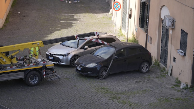 Un carro attrezzi aggancia un’auto scura parcheggiata accanto a un edificio, vicino a un segnale di divieto di fermata.